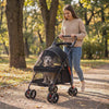 Woman pushing her dog in the black Wander Foldable Dog Stroller along a park path