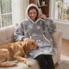 Woman snuggled in the Cuddle paw-print blanket hoodie on the couch with her golden retriever