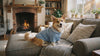 Corgi in a blue plaid-collar cable-knit dog sweater relaxing by a fireplace